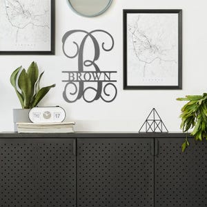 A wall-mounted personalized family name sign, houseplants, framed maps, a round mirror, a digital desk clock, and a geometric-shaped tabletop ornament.