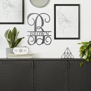 A wall-mounted personalized family name sign, houseplants, framed maps, a round mirror, a digital desk clock, and a geometric-shaped tabletop ornament.