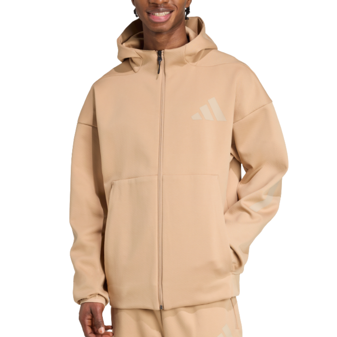 A person wearing a beige Adidas hoodie with a front zipper, large pocket, and logo on the chest and sleeve.