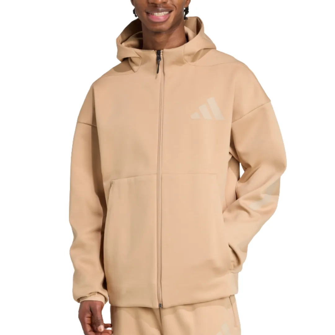 A person wearing a beige Adidas hoodie with a front zipper, large pocket, and logo on the chest and sleeve.