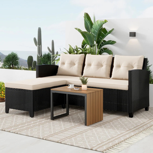 A three-piece outdoor sectional sofa set includes a black wicker L-shaped sofa with cream cushions and a rectangular wooden coffee table. It's placed on a patterned rug in a garden setting with various plants and cacti.