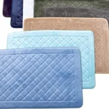 A collection of rectangular bath mats in various colors including blue, light blue, tan, green, and white, with quilted patterns.