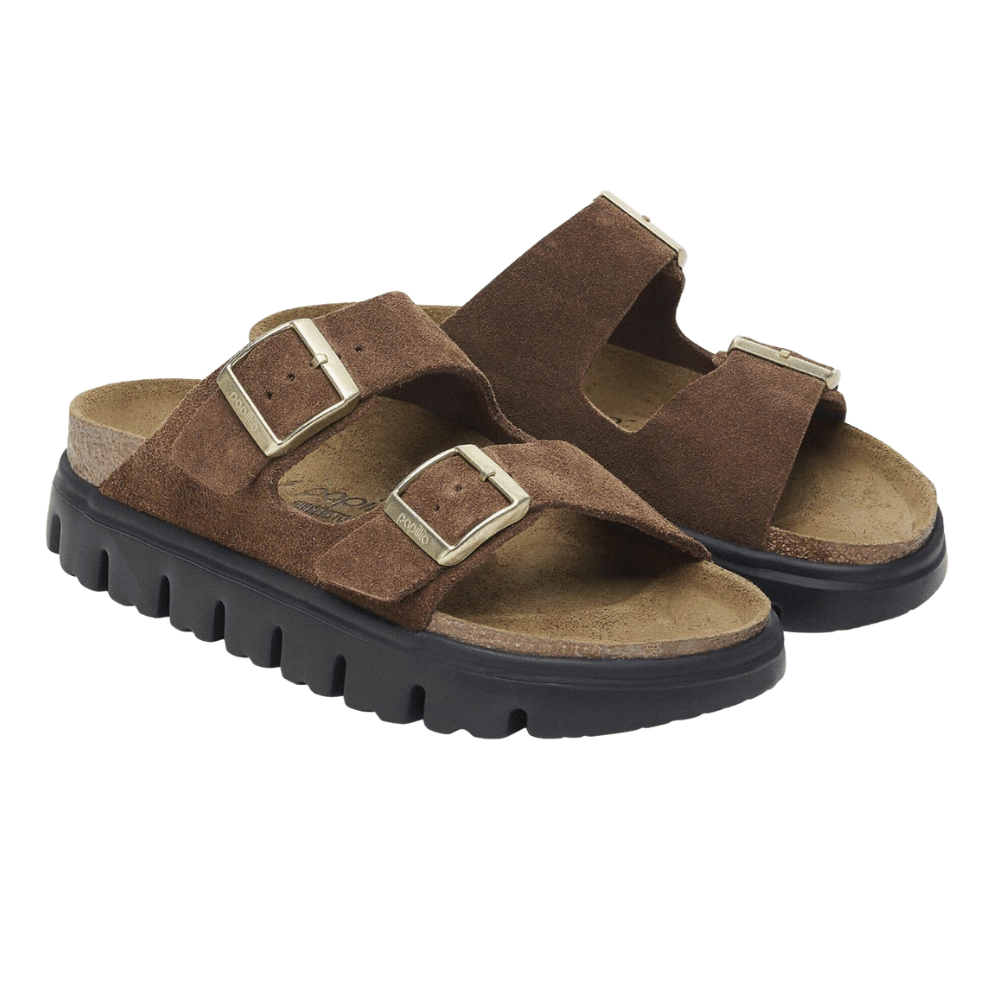 Brown suede sandals with two adjustable straps and gold buckles, featuring a thick black sole with a rugged tread.