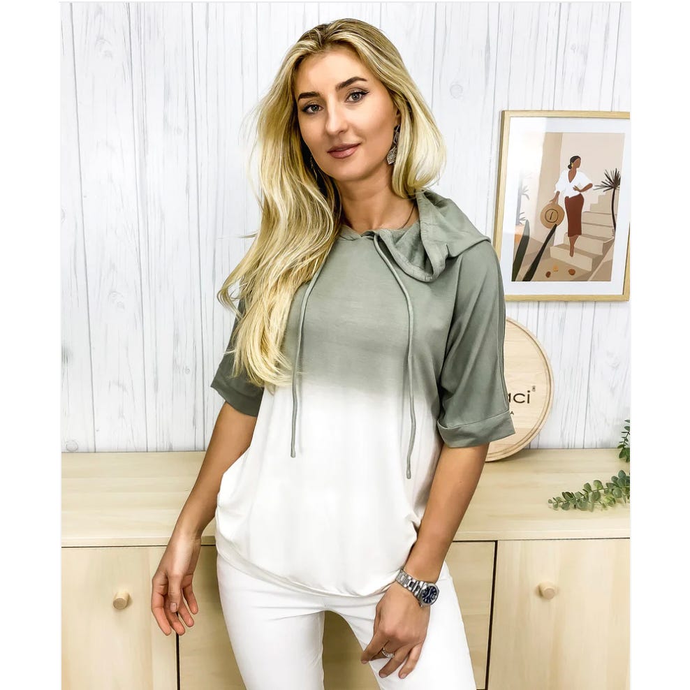 A woman wearing a two-toned hooded top, white at the bottom and olive green on top, with white pants and a watch.