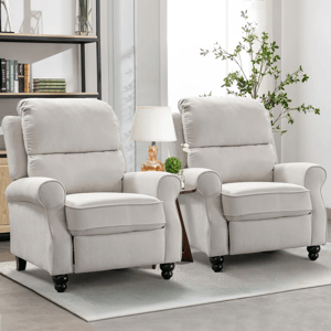 Two light gray upholstered recliners with rounded armrests and dark wooden legs are arranged side by side. A small table with a lamp and plant sits between them, and a bookshelf is visible in the background.