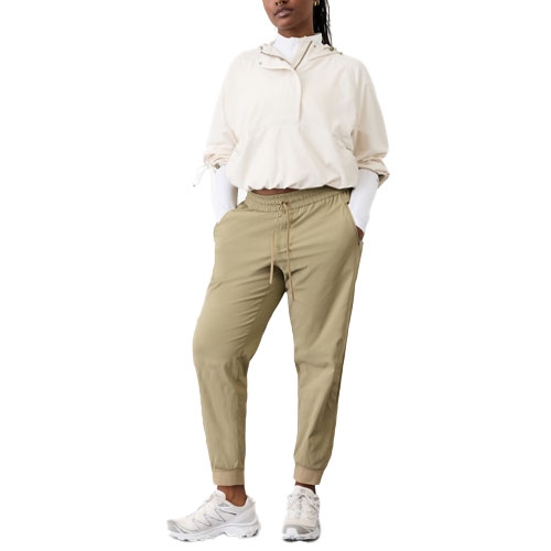 A person wears a beige windbreaker, khaki jogger pants, and white sneakers.