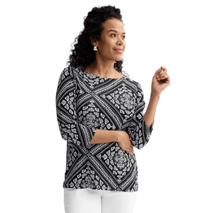 A woman wears a black and white patterned, long-sleeve top paired with white pants.