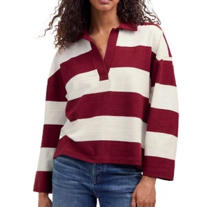 A woman is wearing a long-sleeved rugby-style shirt with maroon and white horizontal stripes, paired with blue jeans.