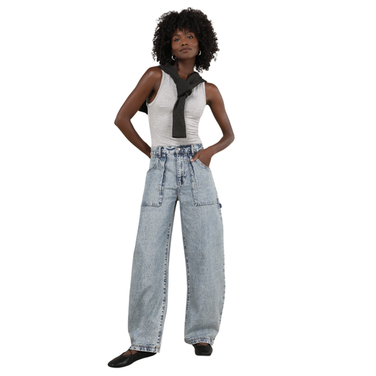 A person is wearing a gray tank top, wide-leg light-wash jeans, a black sweater draped over the shoulders, and black ballet flats.