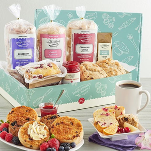 Gift box with English muffins in flavors like blueberry, cherry blossom, and cranberry citrus, alongside jam, coffee, and assorted baked goods, garnished with fresh fruit and a cup of coffee.