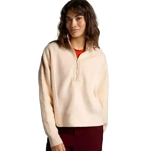 A woman wearing a light peach quarter-zip pullover with a red shirt underneath, paired with maroon pants.