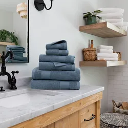 A stack of blue towels is neatly arranged on a marble bathroom counter, with additional towels and bath items on wooden shelves nearby.