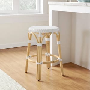 A natural wood counter stool with a round white woven seat and matching white bindings on the legs and footrest. It's positioned next to a white countertop with a light-colored wooden floor beneath.