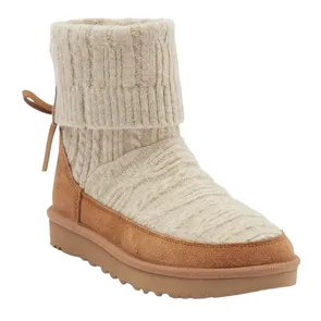 A tan suede boot featuring a ribbed, cream-colored knit upper with a fold-over cuff and tied detailing at the back. It has a flat, textured sole.
