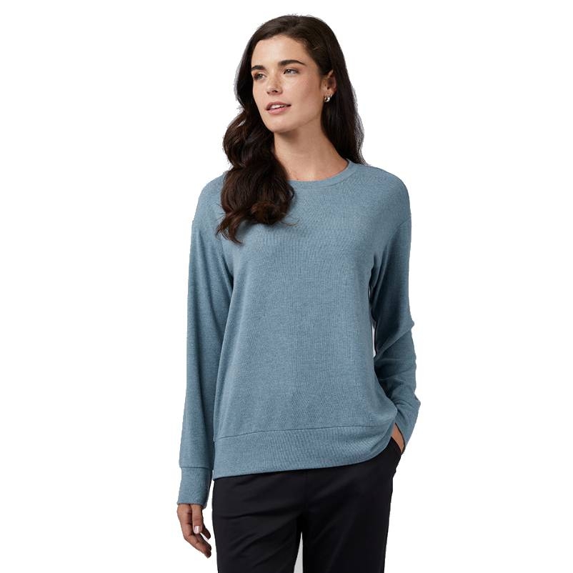 A woman is wearing a light blue crew-neck sweater with long sleeves and ribbed cuffs. The sweater has a relaxed fit, and she is also wearing black trousers.