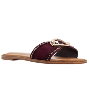 A burgundy slide sandal featuring a wide strap with chain trim and a gold metal accent, set on a flat, tan sole.