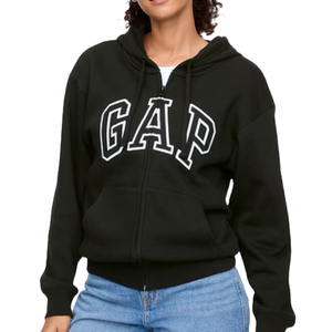 Black hooded sweatshirt with a front zipper and the GAP logo in large white letters on the chest. It features long sleeves and a kangaroo pocket, paired with blue jeans.