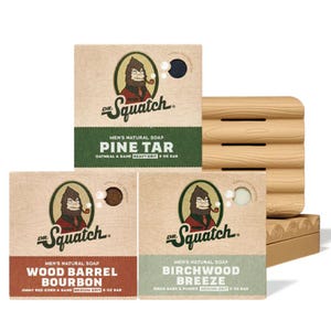 Dr. Squatch men's natural soap bars in scents Pine Tar, Wood Barrel Bourbon, and Birchwood Breeze are shown alongside a wooden soap dish.