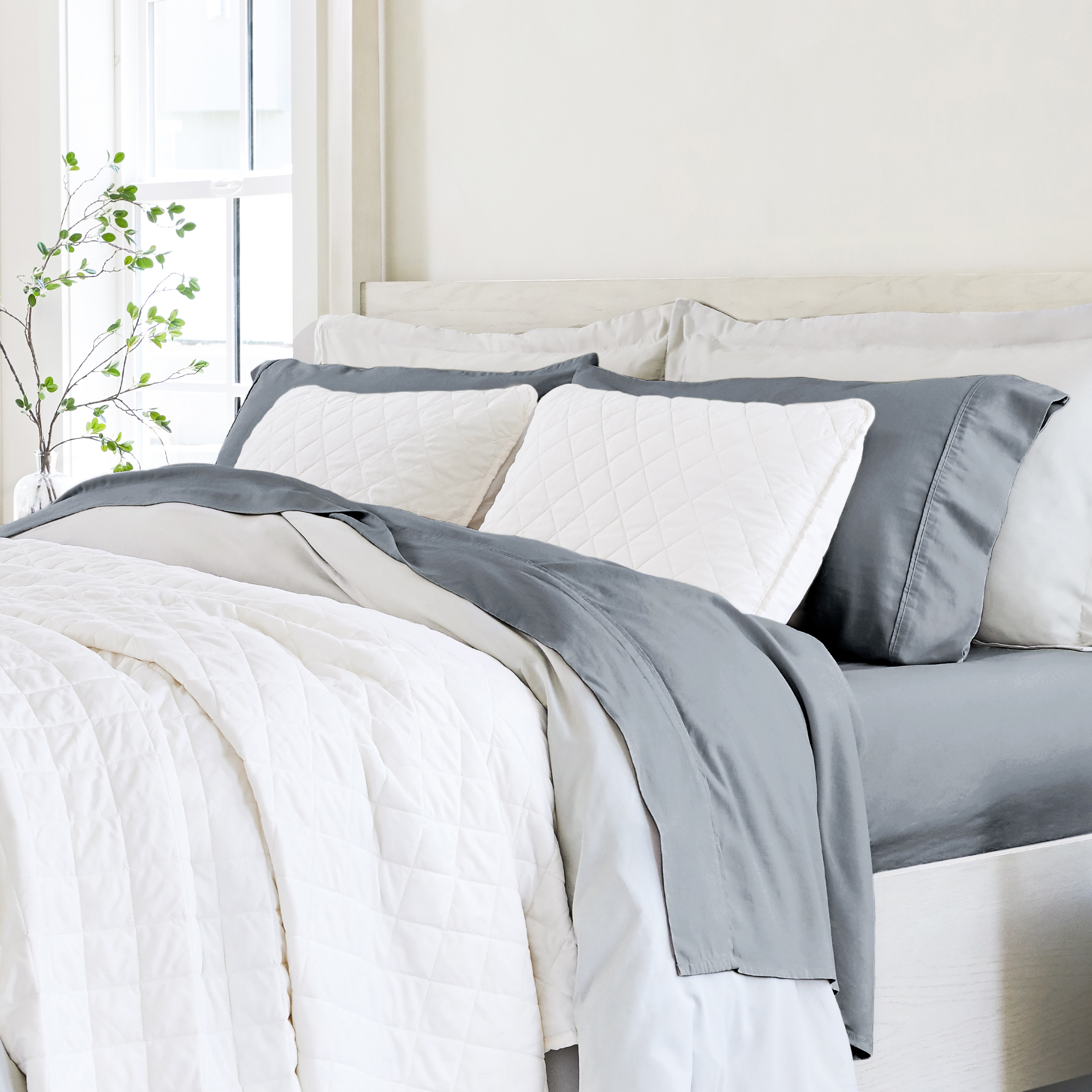 A neatly made bed with white and gray bedding, including pillows, sheets, and a comforter.