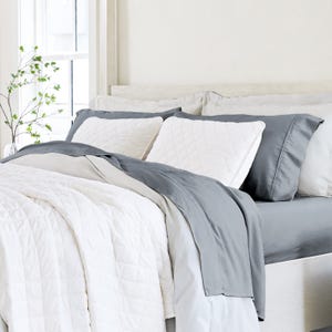 A neatly made bed with white and gray bedding, including pillows, sheets, and a comforter.