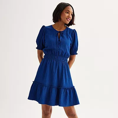 A woman is wearing a short-sleeved, fit-and-flare blue dress with a ruffled hemline and a keyhole neckline detail.