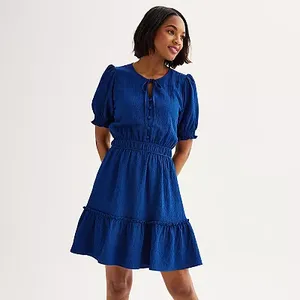 A woman is wearing a short-sleeved, fit-and-flare blue dress with a ruffled hemline and a keyhole neckline detail.
