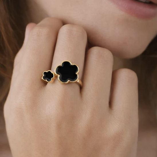 A gold ring with two black clover-shaped stones is worn on a person's hand.