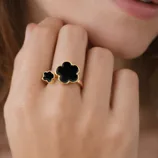 A gold ring with two black clover-shaped stones is worn on a person's hand.