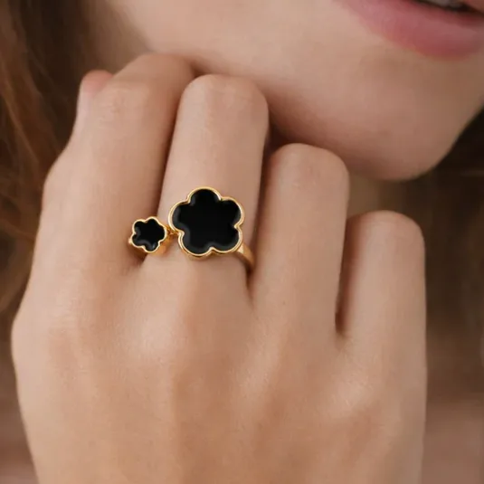 A gold ring with two black clover-shaped stones is worn on a person's hand.
