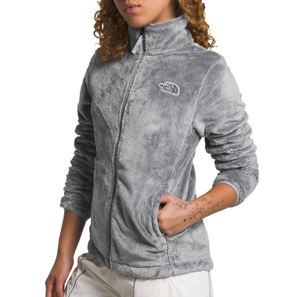 A person is wearing a gray fleece jacket with a logo on the chest, featuring a high collar and front pockets.