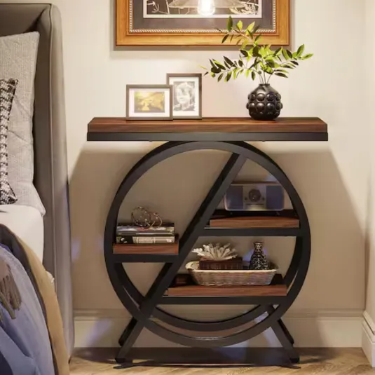Black metal and wood console table with circular design includes two shelves displaying books, a radio, and decorative items. The tabletop holds framed photos and a vase with green foliage.