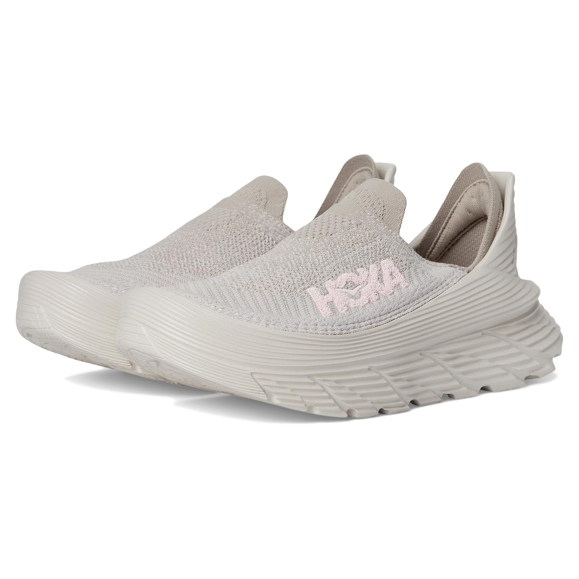 Beige slip-on sneakers with a textured knit upper and cushioned sole, featuring the HOKA logo in light pink.