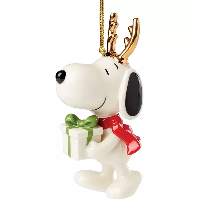 The 2024 Lenox Snoopy Ornament features Snoopy with a red scarf and gold antlers, holding a gift with a green bow. It is designed as a festive hanging decoration.