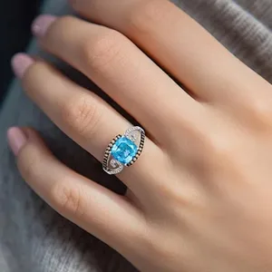 A hand with a silver ring featuring a large blue gemstone in the center, accented by smaller clear stones in a decorative setting.