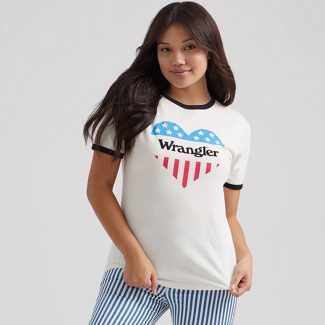 A woman wearing a white ringer tee with a heart-shaped American flag design and the Wrangler logo, paired with blue and white striped pants.