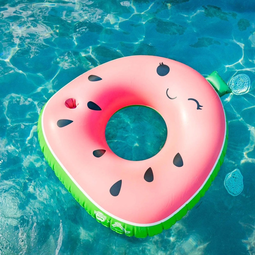 A watermelon-themed inflatable pool float with a smiling face and black seed patterns, featuring a pink center and green outer edge, floating on water.
