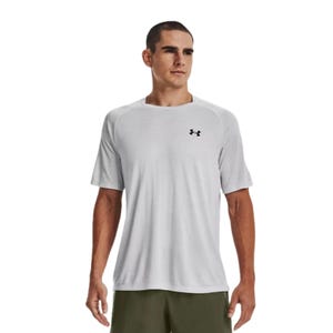 A man is wearing a light gray Under Armour T-shirt with short sleeves and a small logo on the chest, paired with green shorts.