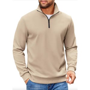 A beige, long-sleeve, quarter-zip pullover paired with blue jeans, featuring a textured fabric and a black zipper, worn over a white undershirt.