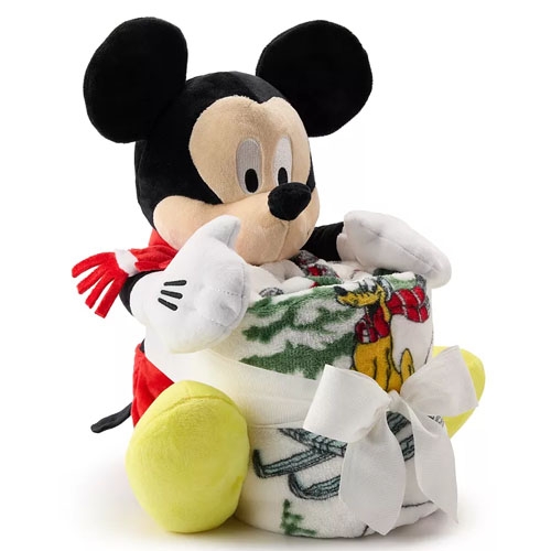 Mickey Mouse plush holding a folded throw blanket featuring a holiday design with a bow. Mickey wears a red scarf, and his signature yellow shoes. The set combines a soft plush toy with a cozy, patterned blanket for added warmth and decoration.