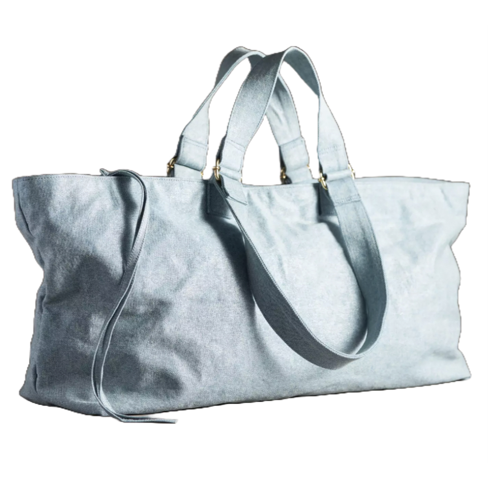 Light blue denim duffel bag with dual handles and a shoulder strap, featuring gold-tone hardware.