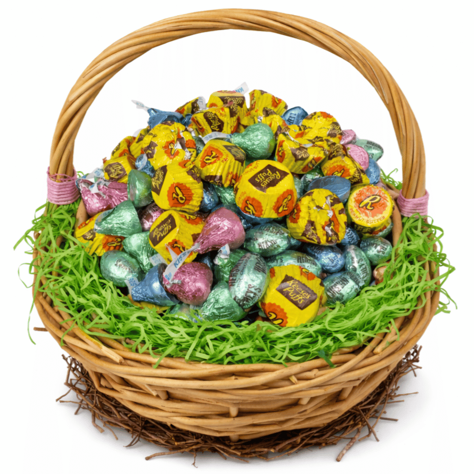 A wicker basket filled with various colored Hershey's Kisses and Reese's Peanut Butter Cups, surrounded by green decorative grass.