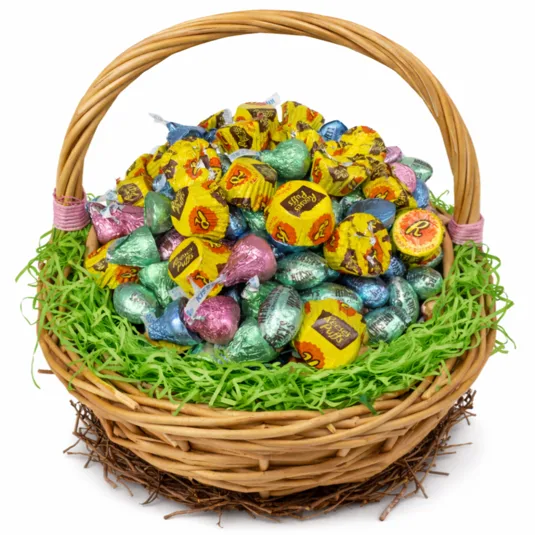 A wicker basket filled with various colored Hershey's Kisses and Reese's Peanut Butter Cups, surrounded by green decorative grass.