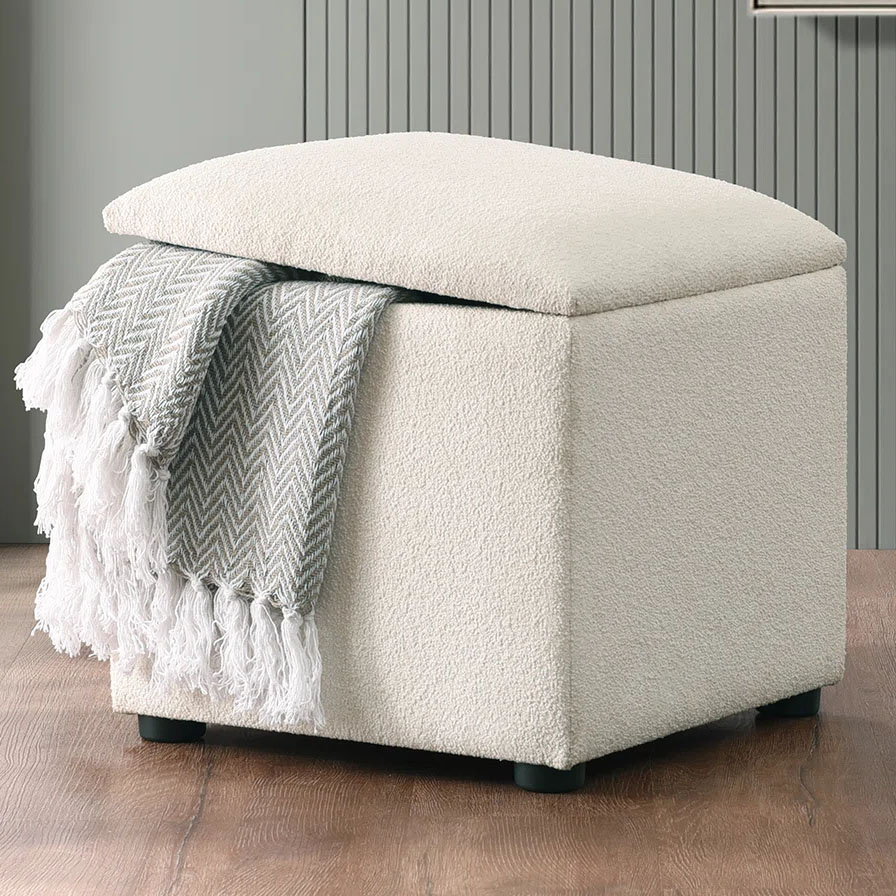 Cream-colored boucle storage ottoman with a removable lid, featuring a hidden interior for storage. Comes with a draped gray and white chevron-patterned throw blanket.
