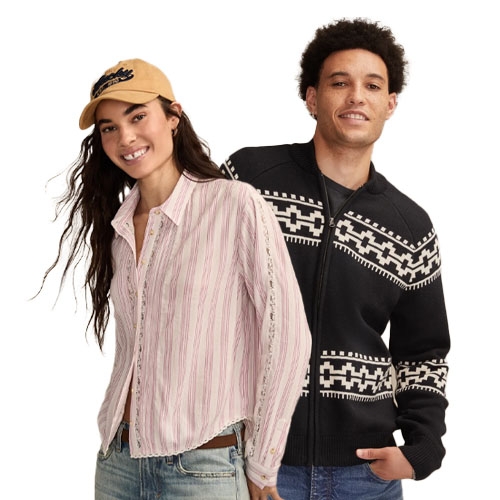 A woman in a striped button-up shirt, jeans, and a cap stands next to a man wearing a black and white patterned sweater.