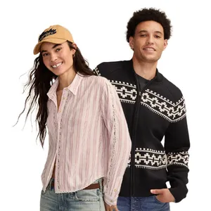 A woman in a striped button-up shirt, jeans, and a cap stands next to a man wearing a black and white patterned sweater.