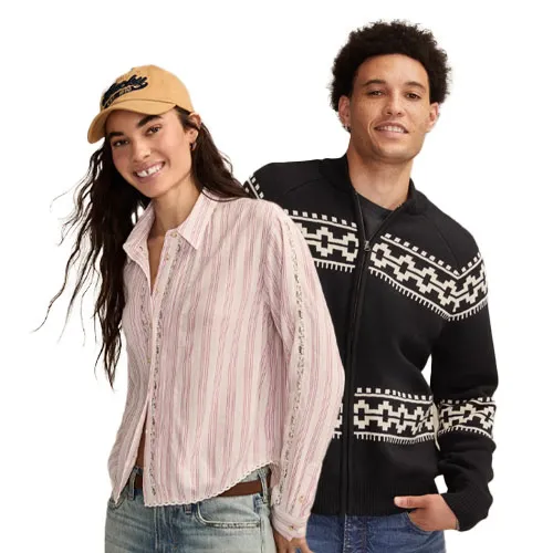 A woman in a striped button-up shirt, jeans, and a cap stands next to a man wearing a black and white patterned sweater.