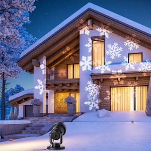 A rotating snowflake projector casts large white snowflake patterns onto the front of a house, adding a festive touch to the snowy winter scene.