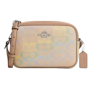 A Coach crossbody bag with a light tan strap, featuring a pastel multi-color signature pattern and a silver logo.