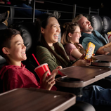 A group of people enjoy a movie in a theater with reclining seats, holding snacks like popcorn, soft drinks, and M&M's.