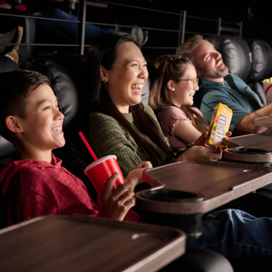 A group of people enjoy a movie in a theater with reclining seats, holding snacks like popcorn, soft drinks, and M&M's.